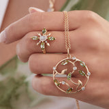 Model wearing tourmaline and moonstone ring in 14K gold holding a round pendant with gold leaves, tourmaline and diamonds
