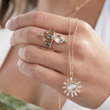 Model holding moonstone and diamond pendant wearing moonstone and green sapphire crown ring