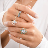 Model wearing moonstone and green sapphire rings and holding moonstone and diamond pendant