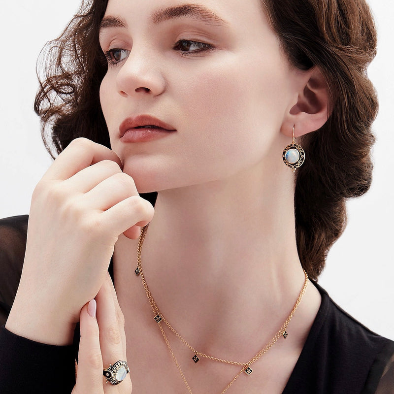 Model wearing moonstone earrings with black enamel and gold scrolling