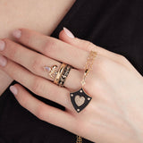 Model holding black enamel and diamond heart shield pendant with fleur de lis ring set in enamel and 14K gold