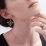 Model wearing fleur de lis and moonstone earrings with black enamel in 14K gold